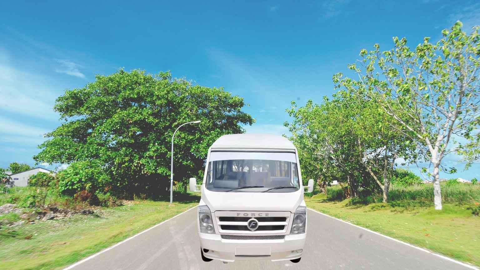 A white Force Tempo Traveller van is parked on the green roadside. It’s perfect if you need to book a group cab in Madurai.