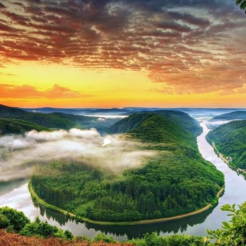 A river winds through green hills as the sun rises, painting the sky gold and creating a soft mist over the water.