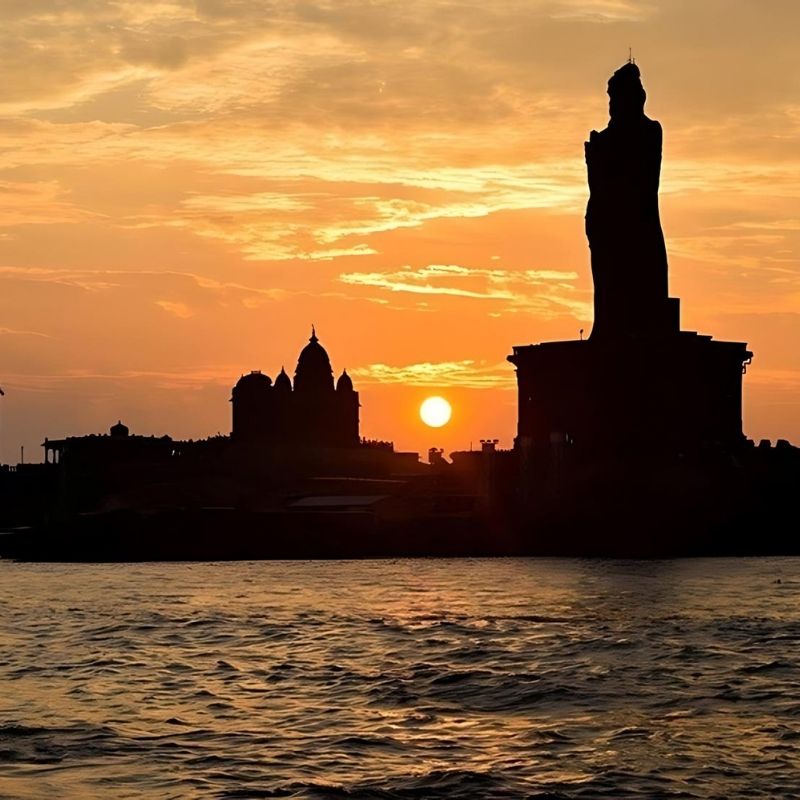 Kanyakumari's Vivekananda Rock and Thiruvalluvar Statue at sunrise, with an orange sky and sea view.
